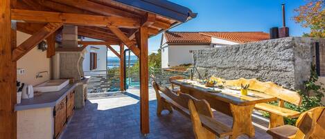 A covered outdoor dining area with wooden furniture and a stone wall.