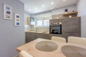 Eine moderne Küche mit grauen Schränken, einem eingebauten Backofen und einem Essbereich mit einem Holztisch und zwei beigen Stühlen.