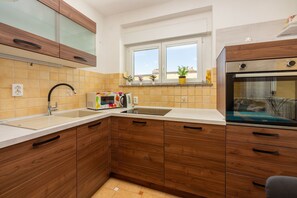 Una cocina con armarios de madera, microondas, hervidor y ventana con plantas.