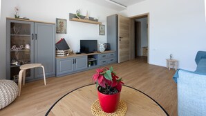 Een moderne woonkamer met grijze kasten, een televisie en een rode plant in pot.