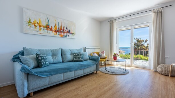 Een moderne woonkamer met een blauwe bank, een kleine ronde tafel en uitzicht op de omgeving door een schuifdeur.