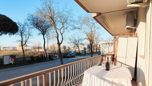 A balcony with a table set for two, overlooking a road and trees. - Studio Apartment Near Piazza Nember (Jesolo)