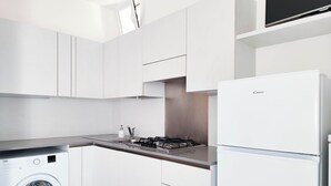 A compact kitchen with white cabinets, a built-in washing machine, a gas stove, and a refrigerator. - Studio Apartment Near Piazza Nember (Jesolo)