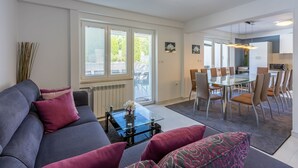 Ein modernes Wohnzimmer mit einem grauen Sofa, einem Glastisch und einem Essbereich mit Tisch und Stühlen.