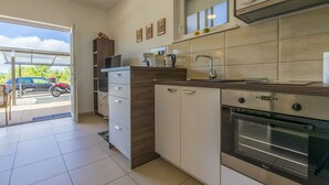 Eine moderne Küche mit Einbauofen, Mikrowelle und Kaffeemaschine. Über der Spüle befindet sich ein Fenster und eine Tür führt zur Garage.