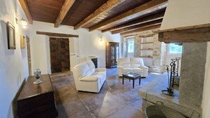 Un vaste espace de vie agrémenté d’une cheminée en pierre, de canapés en cuir blanc et d’un plafond en bois.