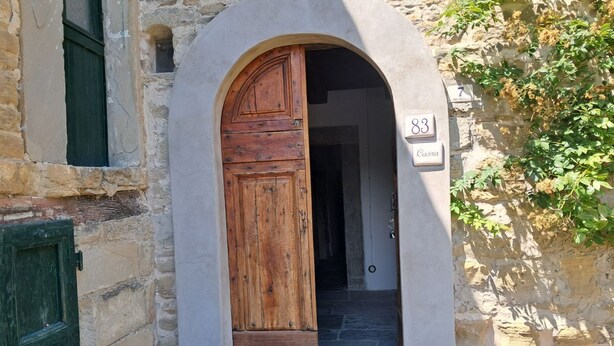 Une porte en bois en forme d’arc, adossée à un mur en pierre, et sur laquelle est fixée une plaque numérotée.