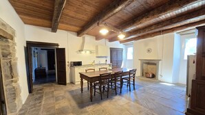 Une cuisine spacieuse avec une grande table en bois, un sol en pierre et un plafond rustique.
