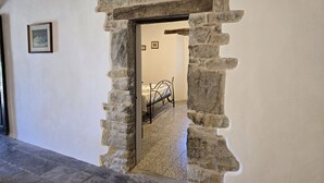 Un arc en pierre mène à une chambre à coucher où se trouvent un lit et un tableau encadré au mur.
