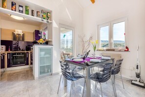 A modern kitchen with a built-in oven and a dining area with a glass table and metal chairs. - Stunning two-storey penthouse with hot tub and panoramic views (Crikvenica)