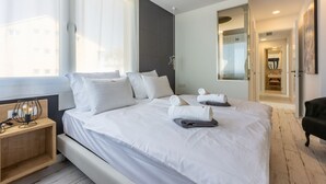 Ett modernt hotellrum med en stor säng, vita sängkläder, ett nattduksbord med en lampa och utsikt över staden genom fönstret.