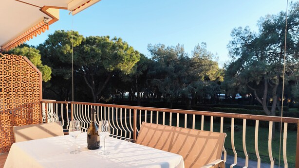 A table set with a bottle and glasses, a white tablecloth, and a view of trees and a fence. - Comfortable Studio Near Piazza Nember (Jesolo)