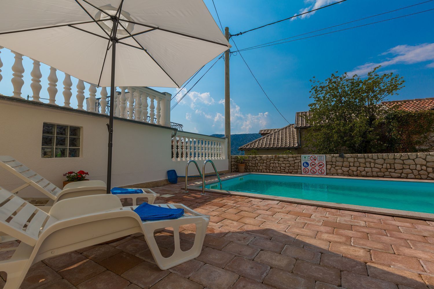A pool area with a white umbrella, lounge chairs, and a stone wall.