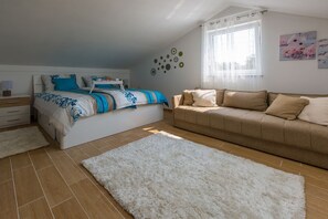 Ein Schlafzimmer mit einem Bett, einem Sofa, einem weißen, flauschigen Teppich und einem Fenster mit Vorhängen.