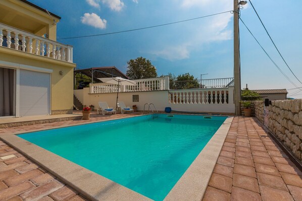Ein rechteckiger Pool mit gefliestem Rand, umgeben von einer Pflasterterrasse.