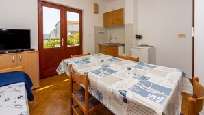 A compact room with a bed, a TV, a dining table with chairs, a kitchenette, and a door leading to a balcony. - Quiet studio apartment just 250 metres from the beach with sea view, parking space, barbecue (Novi Vinodolski)