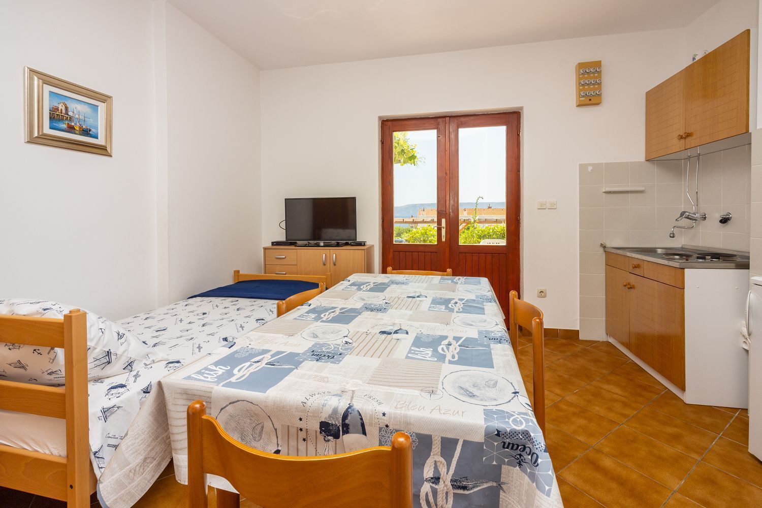 A small, tidy room with a bed, a table, and a TV. There's a window with a view of buildings and greenery.
