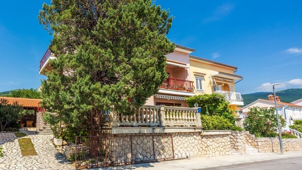 A two-story building with a balcony and a stone wall. - Quiet studio apartment just 250 metres from the beach with sea view, parking space, barbecue (Novi Vinodolski)