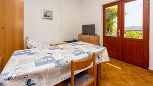 A room with a bed, a table with a quilt, a TV on a wooden cabinet, and a door leading to an outdoor area with a view. - Quiet studio apartment just 250 metres from the beach with sea view, parking space, barbecue (Novi Vinodolski)