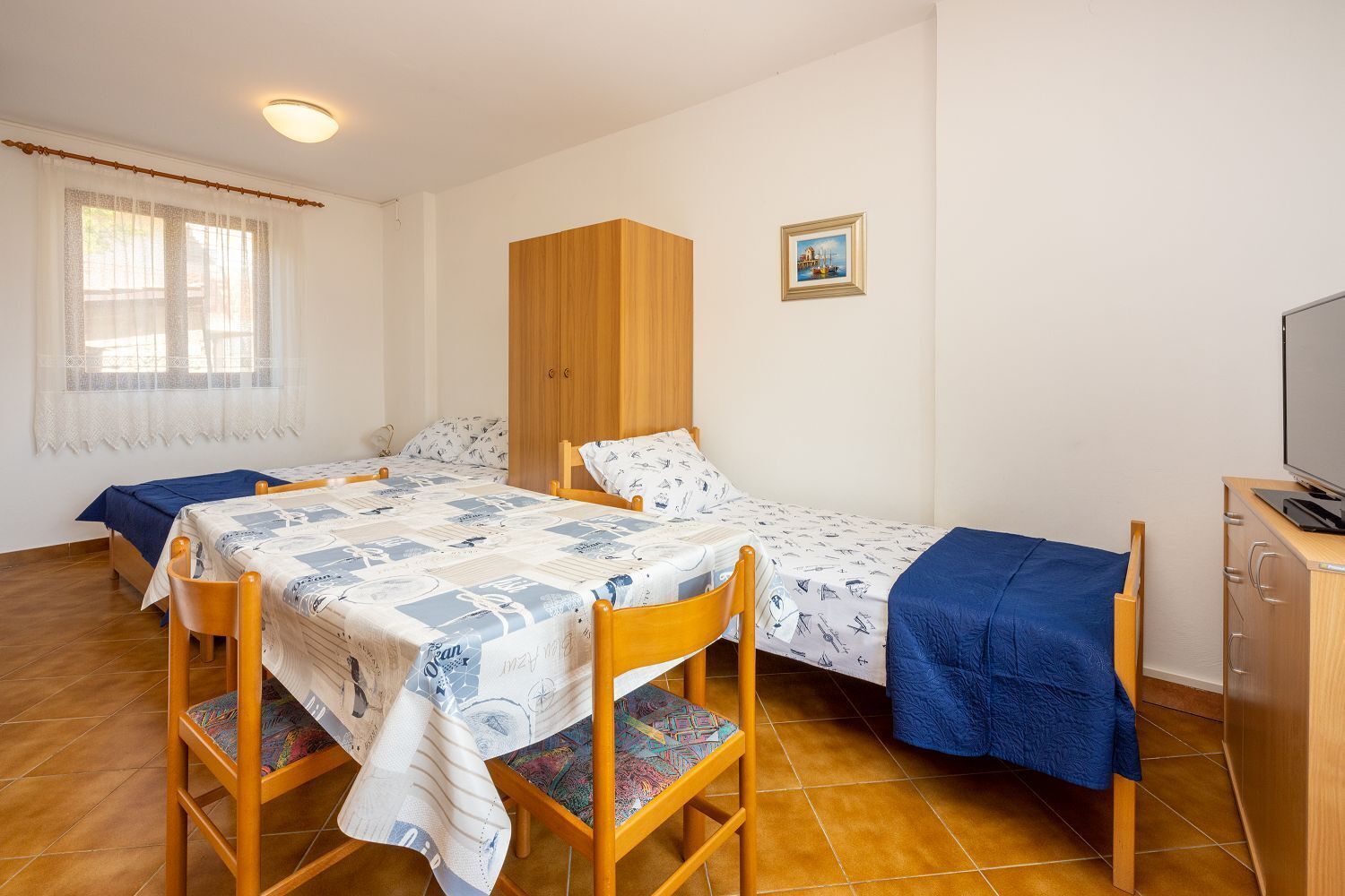 Ein Zimmer mit zwei Einzelbetten, einem Holzschrank, einem Fernseher und einem Fenster mit Vorhängen.