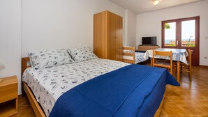 A bedroom with a bed, a wooden wardrobe, a desk with a chair, and a television. - Quiet studio apartment just 250 metres from the beach with sea view, parking space, barbecue (Novi Vinodolski)