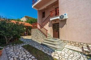 Ein Gebäude mit einer Steintreppe, die zu einer Tür führt, ein kleiner Garten mit einem Baum und ein strahlend blauer Himmel.