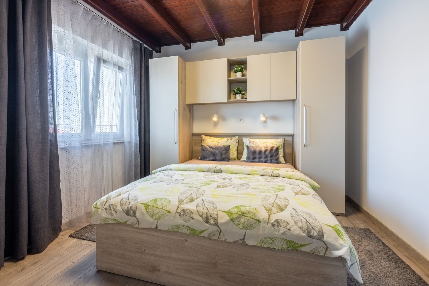 Une chambre à coucher avec un lit, une tête de lit en bois, des rangements intégrés et une fenêtre avec des rideaux.