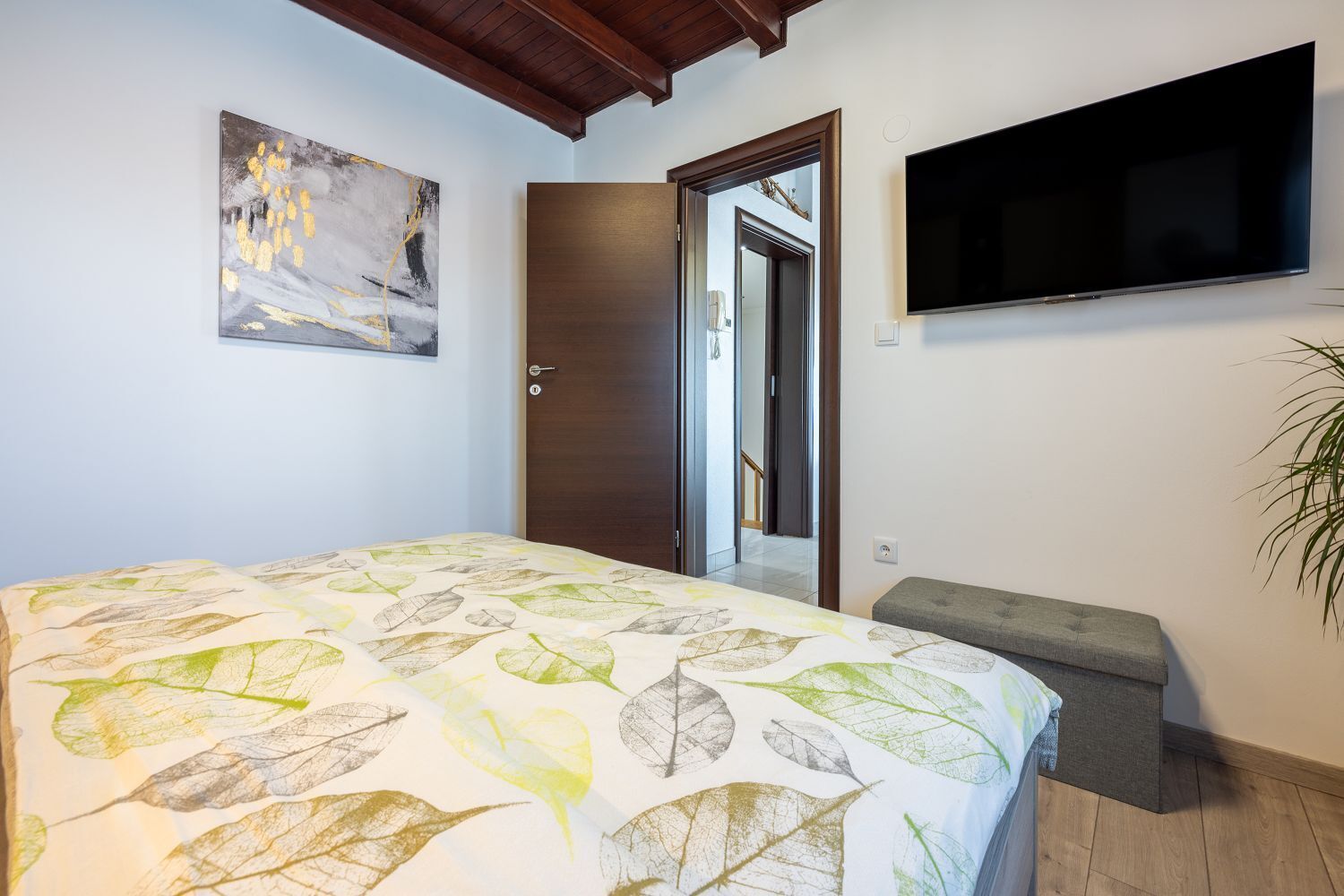 Een slaapkamer met een bed, een aan de muur bevestigde televisie, een deur en een trap naar een andere kamer.