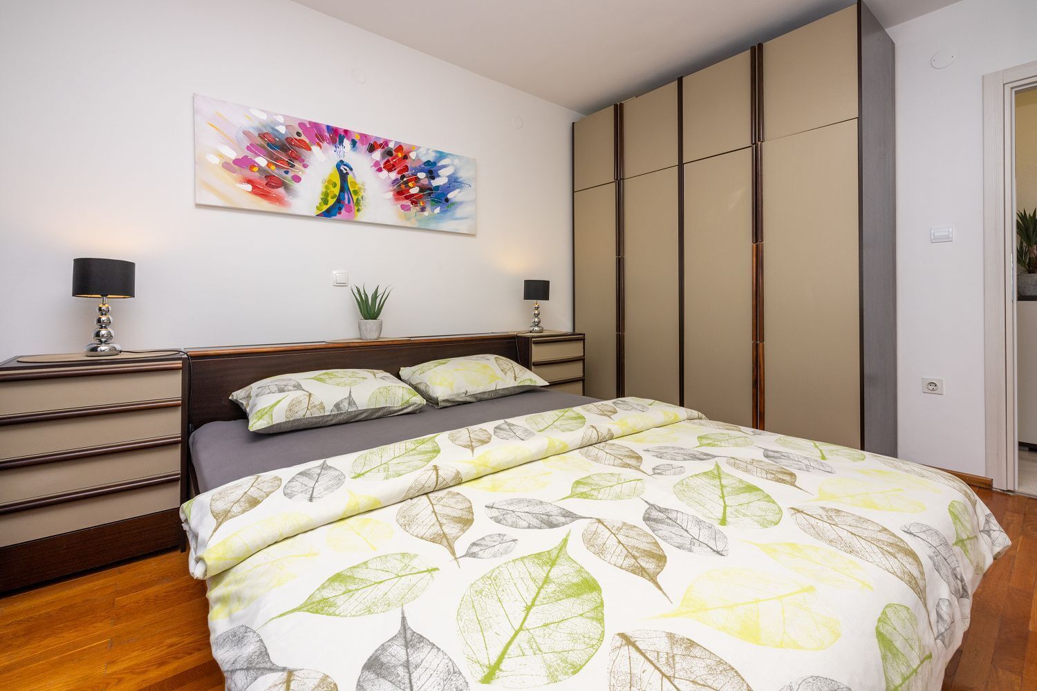 Un dormitorio con una cama, una mesita de noche, una lámpara, una planta y un armario.