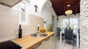 A modern kitchen with a wooden countertop, stainless steel sink, and a black induction cooktop. There is a dining area with a table and chairs, and a view of the outside through large windows.