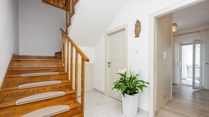 A wooden staircase with a white wall and a white door. There is a potted plant with white flowers next to the door.