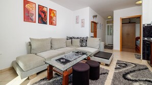Un soggiorno moderno con un divano componibile, un tavolino in vetro e una cucina visibile attraverso una porta aperta.