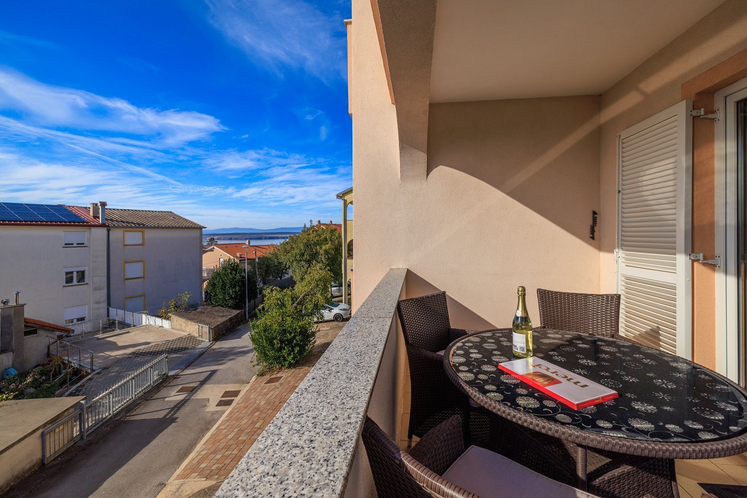 A balcony with a table and chairs, a bottle of champagne, and a book.