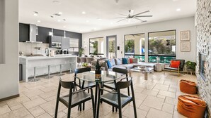 Een moderne keuken met een centraal eiland, een eethoek met een glazen tafel en een zithoek met een bank en stoelen.