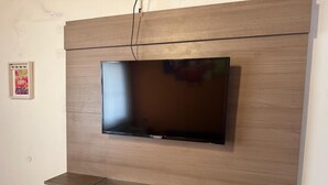 A wall-mounted TV with a wooden panel design and a glass shelf below.