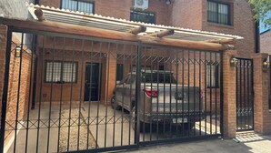 A gated parking area with a brick building, a covered carport, and a parked SUV.