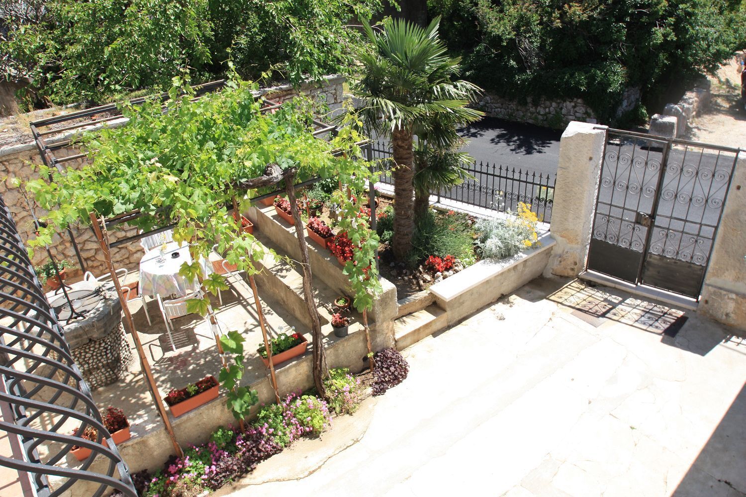 A rooftop garden with a grill, potted plants, and a view of a stone wall and trees.