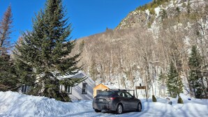 Un coche estacionado frente a una casa con una entrada cubierta de nieve y una montaña al fondo.