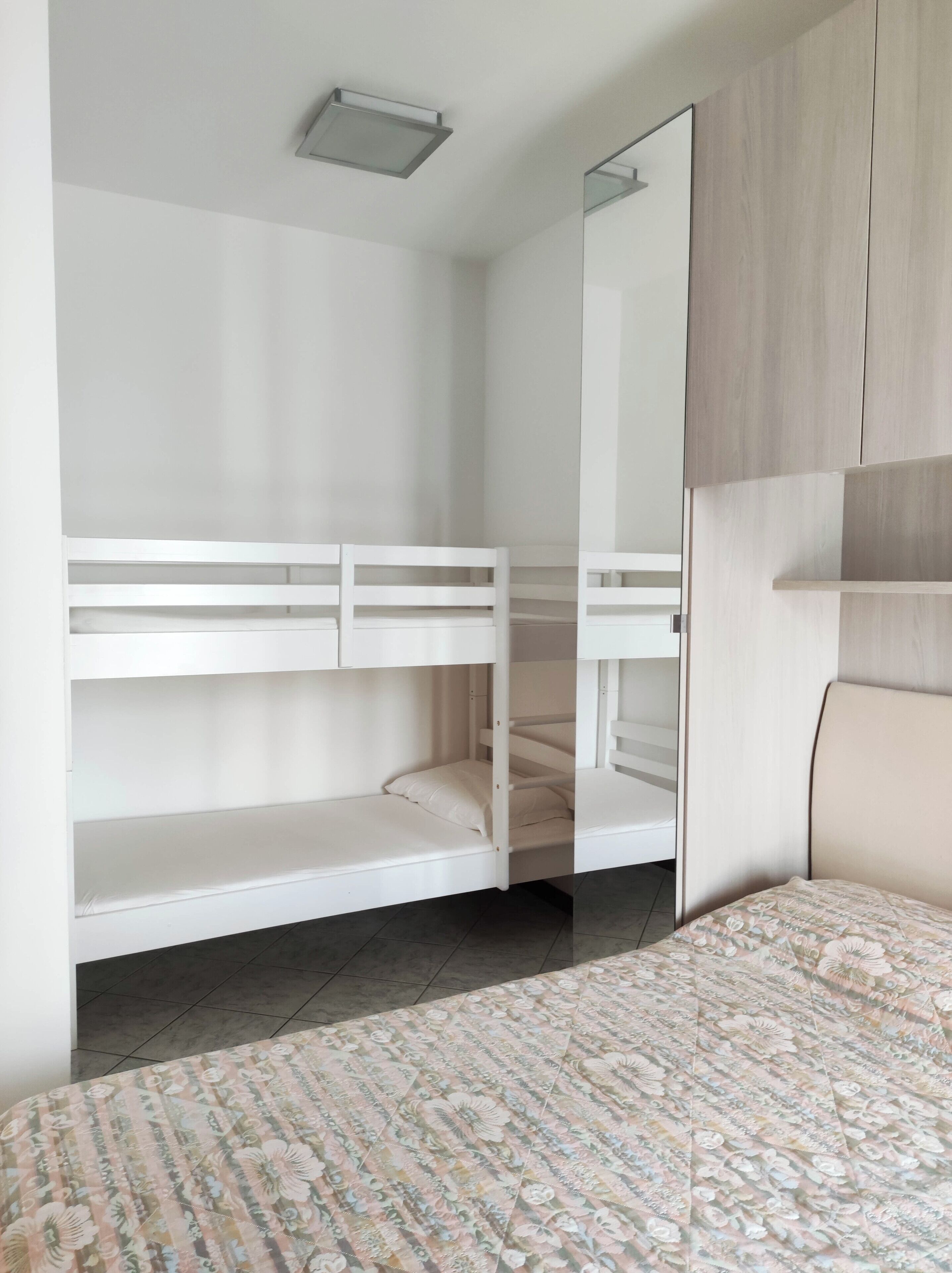 A bedroom with a bunk bed, a large mirror, and a floral bedspread.