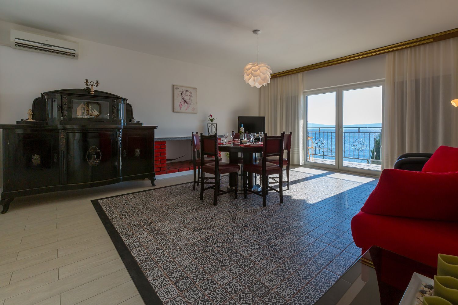 Un soggiorno con zona pranzo, un divano rosso, un mobile nero e un'ampia finestra vista mare.