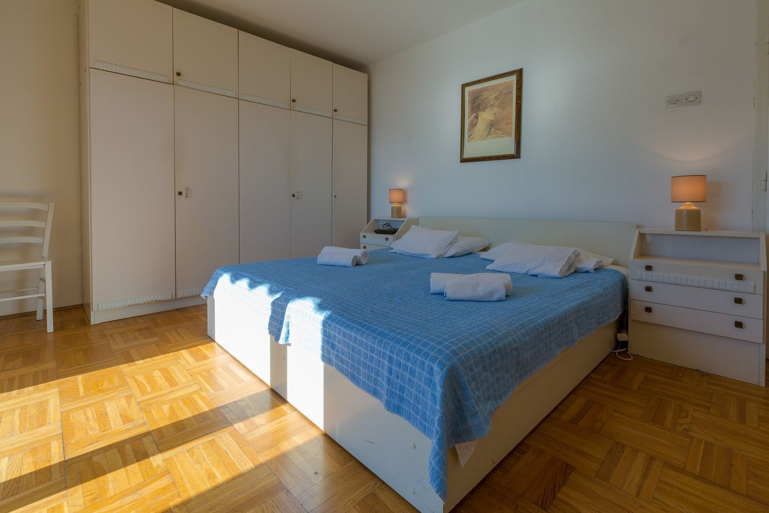 A bedroom with a bed, bedside lamps, a chair, and a wardrobe.