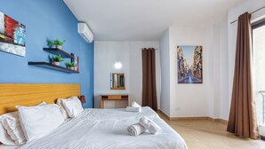 Hotellihuone, jossa on sänky, työpöytä, tuoli, peili, ikkuna verhoilla ja seinä, jossa on taulu.