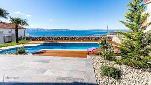 A pool area with a view of the sea, stone walls, and a wooden deck. - Charming apartment with pool, sea view, garage, washing machine (Klenovica)