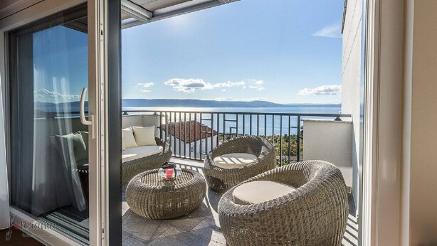 A balcony with wicker furniture, a glass door, and a view of the sea and mountains. - Charming apartment with pool, sea view, garage, washing machine (Klenovica)
