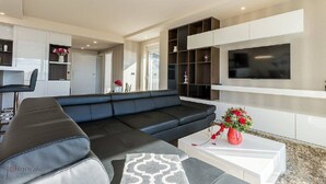 A modern living room with a black sectional sofa, a white coffee table, and a TV mounted on the wall. - Charming apartment with pool, sea view, garage, washing machine (Klenovica)