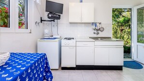 Une cuisine compacte équipée d’une cuisinière à gaz, d’une machine à café et d’un téléviseur fixé au-dessus du plan de travail.