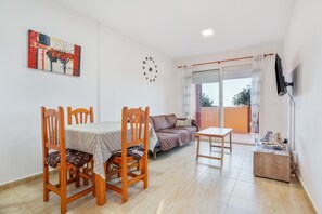 Une pièce comprenant une table à manger, des chaises, un canapé, un téléviseur et une fenêtre avec des rideaux.
