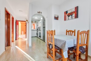 Un espace repas avec une table et des chaises, une cuisine à l’arrière-plan et un couloir menant à d’autres pièces.