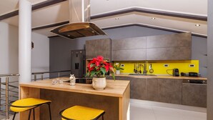Una cocina moderna con una isla de madera, dos taburetes amarillos, una planta en maceta y una campana extractora de acero inoxidable.
