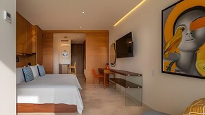 A modern hotel room with a bed, a desk, and a chair. There is a television mounted on the wall and a painting above the desk. - New Studio at la Cruz de Huanacaxtle (Cruz de Huanacaxtle)